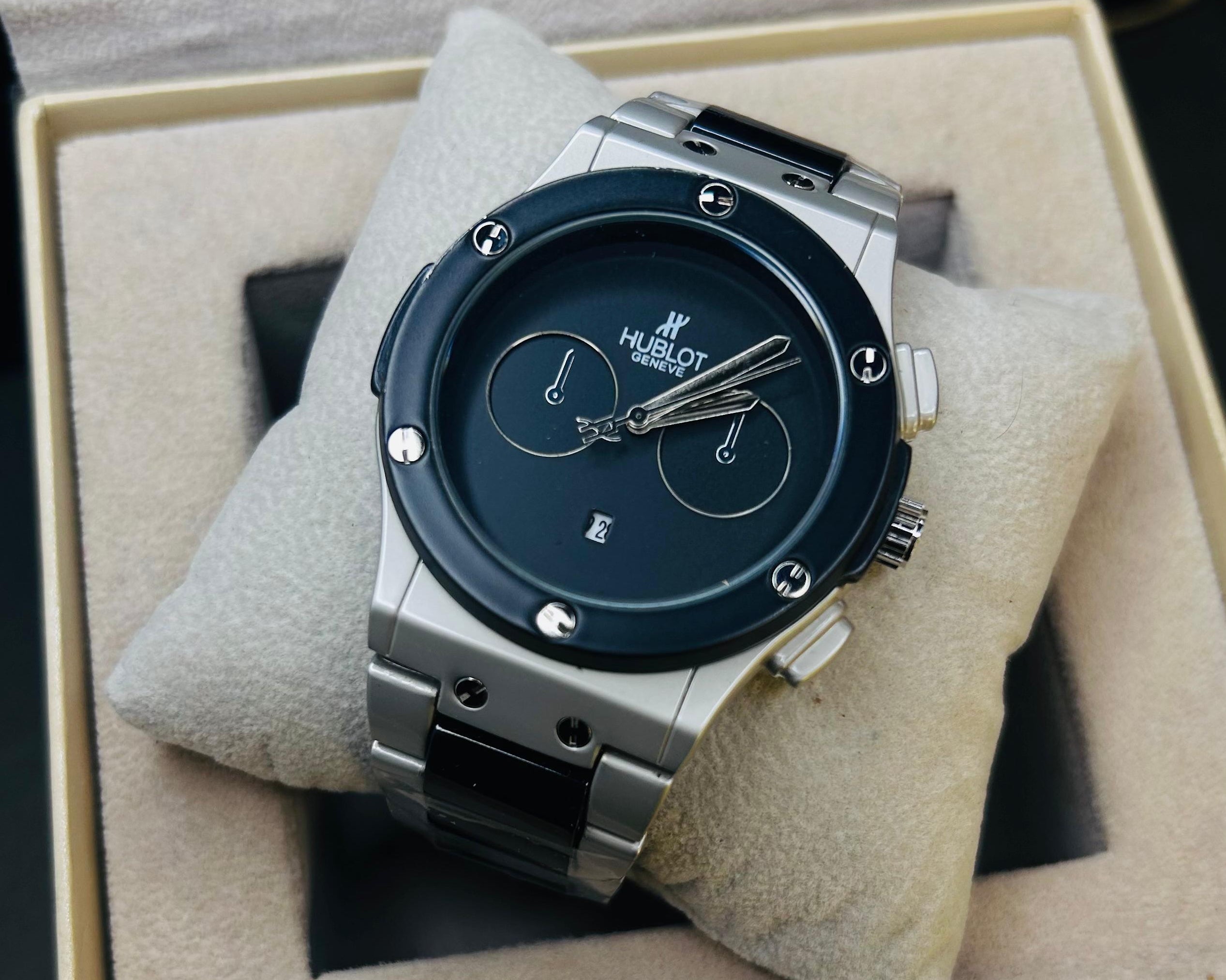 Hublot watch with a dark blue dial and silver-toned case, displayed on a beige cushion inside its presentation box.