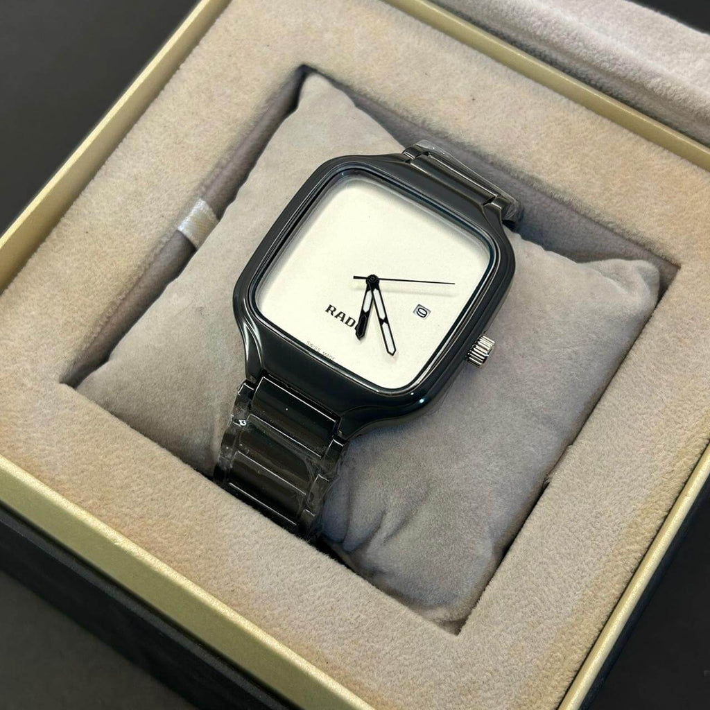 A Rado analog watch with a square black case, white dial, and black metal link bracelet, presented inside a beige cushioned watch box.
